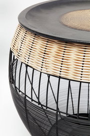 Nahaufnahme eines modernen Beistelltisches mit schwarzem Metallgestell und geflochtenem Rattan-Element, seitliche Perspektive.