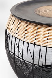 Nahaufnahme eines modernen Beistelltisches mit schwarzem Metallgestell und geflochtenem Rattan-Element, seitliche Perspektive.
