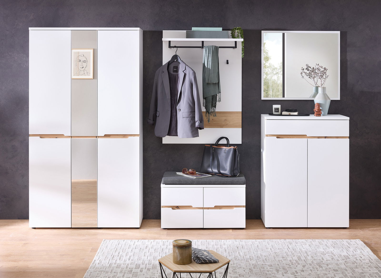 Moderne Garderobenkombination in Weiß mit Holzdetails, bestehend aus einem großen Schrank, einem Garderobenpaneel mit Haken und Ablage, einer Sitzbank mit Stauraum und einem Spiegel. Frontalansicht.