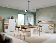 Moderner Esstisch in einem stilvollen Esszimmer mit grüner Wand, umgeben von eleganten Stühlen und Vitrinen, aus der Perspektive des Raumes betrachtet.