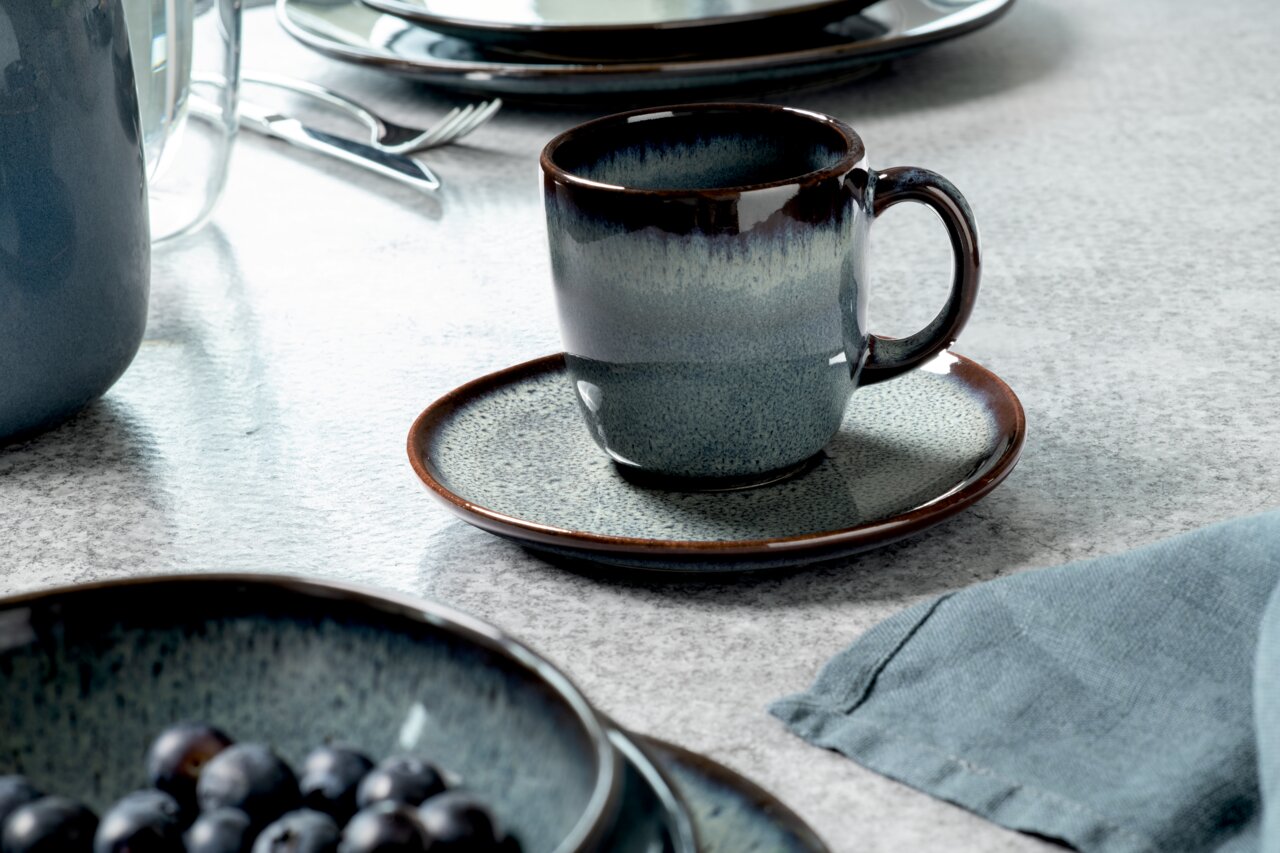 Like by Villeroy & Boch Untertasse LAVE GRIS Kaffeeuntertasse Lave grau mit passender Tasse, seitliche Perspektive auf einem gedeckten Tisch.