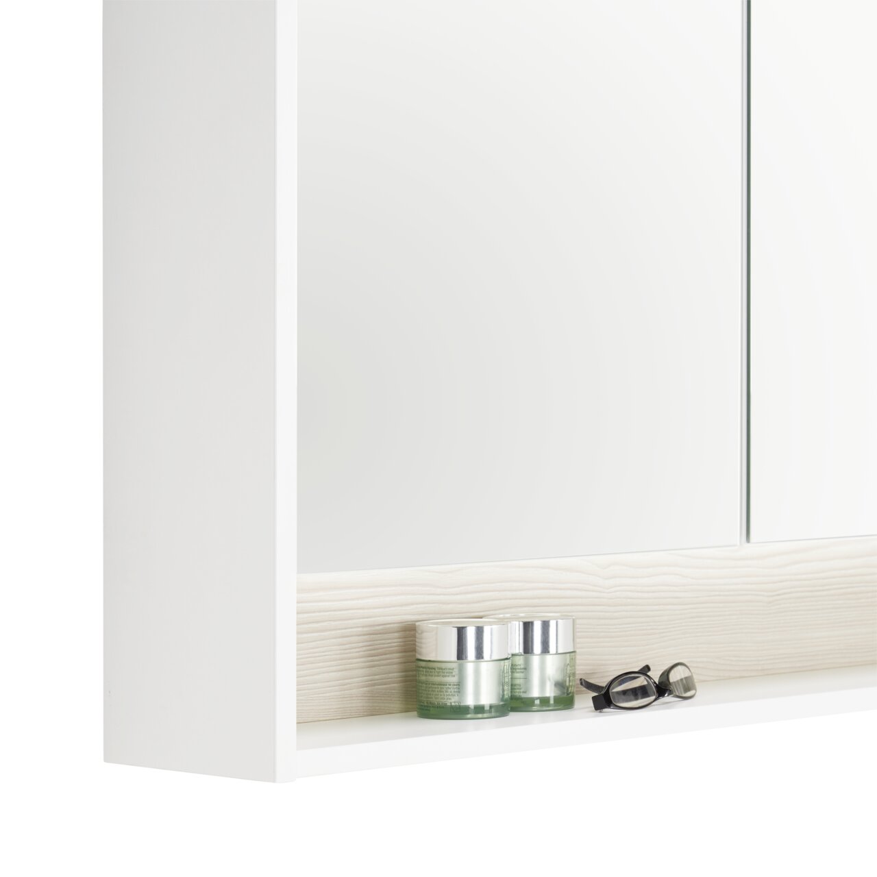 Nahaufnahme eines weißen Spiegelschranks mit zwei Glastiegeln und einer Brille auf einem Regalbrett.