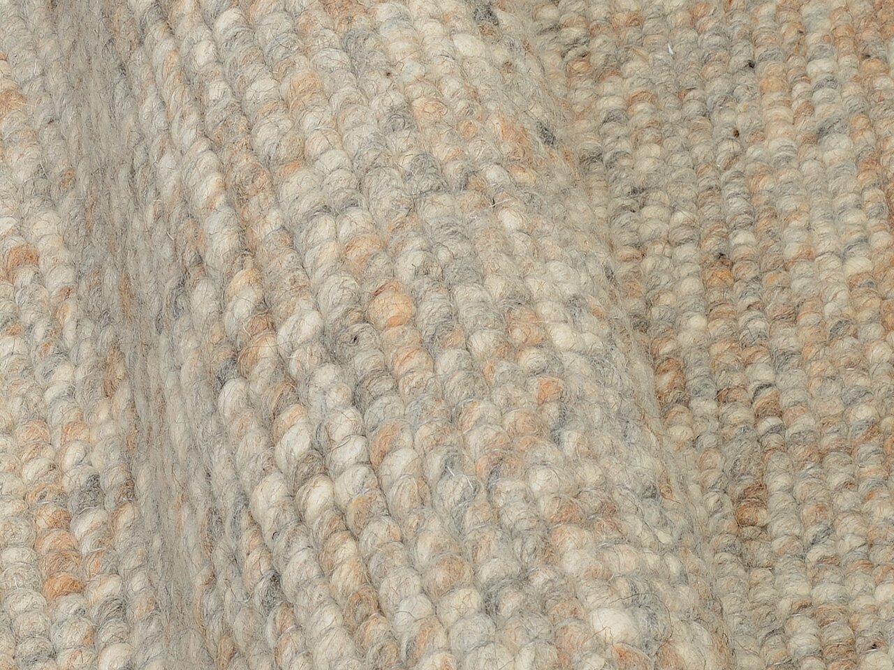 Nahaufnahme eines handgewebten Teppichs mit grober Textur in natürlichen Beige- und Grautönen, seitliche Perspektive.