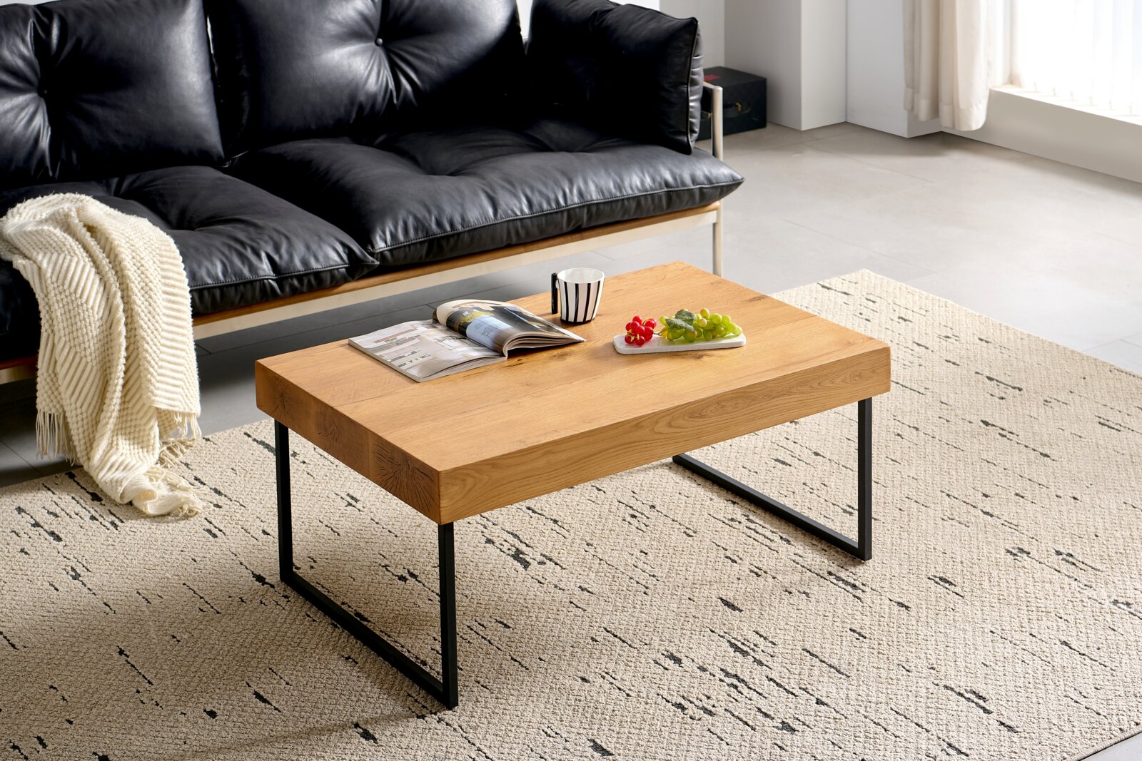 Moderne houten salontafel met metalen poten, van schuin bovenaf gefotografeerd, op een tapijt met patroon voor een zwarte leren bank.