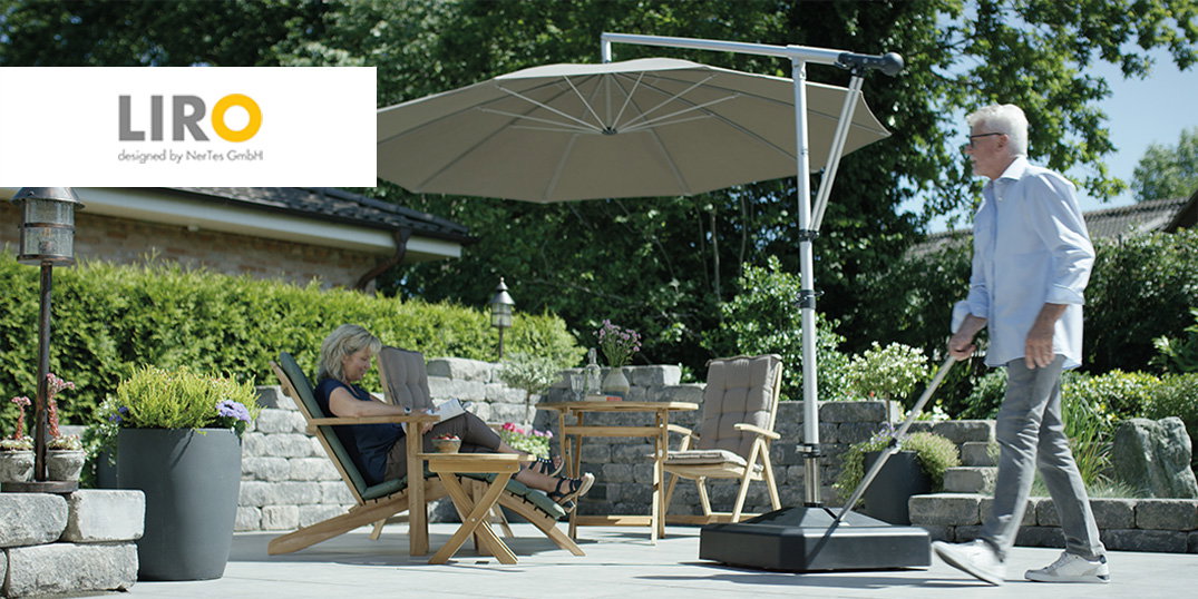 Een kleine zithoek in de open lucht, met op de achtergrond een rustieke stenen muur en een grote parasol van het merk Liro.