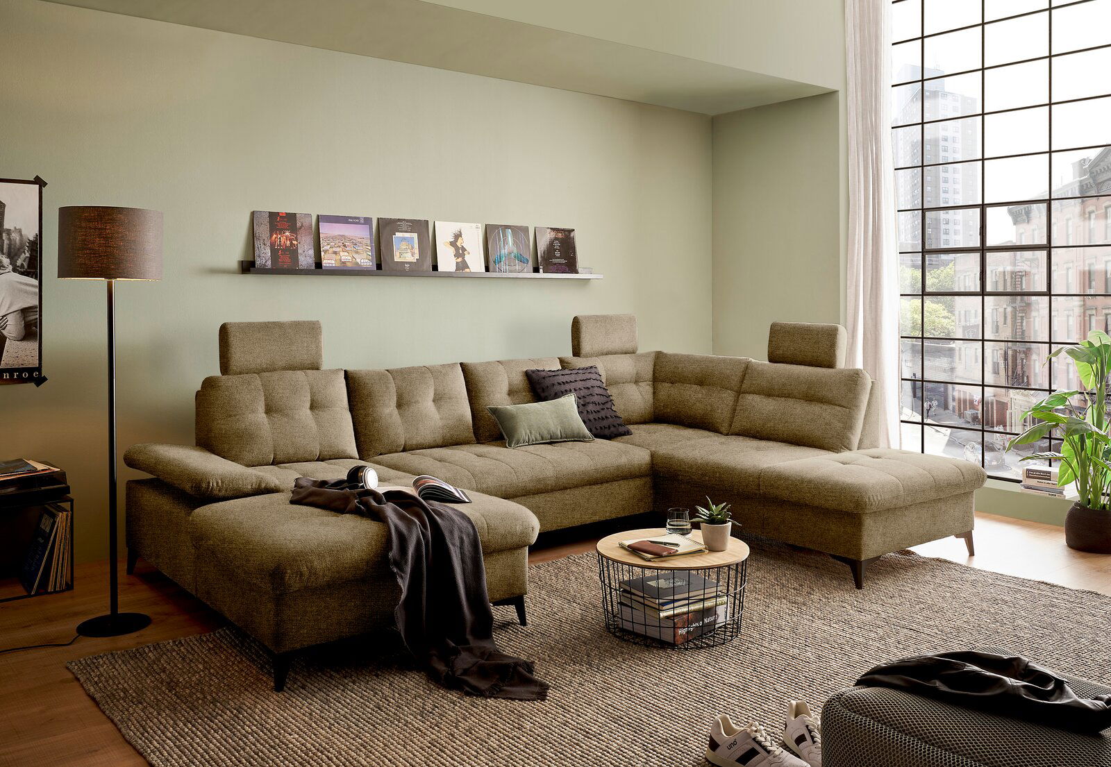 Gemütliche U-förmige Wohnlandschaft in einem modernen Wohnzimmer mit großen Fenstern, die einen Blick auf die Stadt bieten. Perspektive von vorne links.