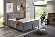 Modernes Boxspringbett in einem stilvollen Schlafzimmer mit Holzverkleidung und großen Fenstern, seitliche Perspektive.