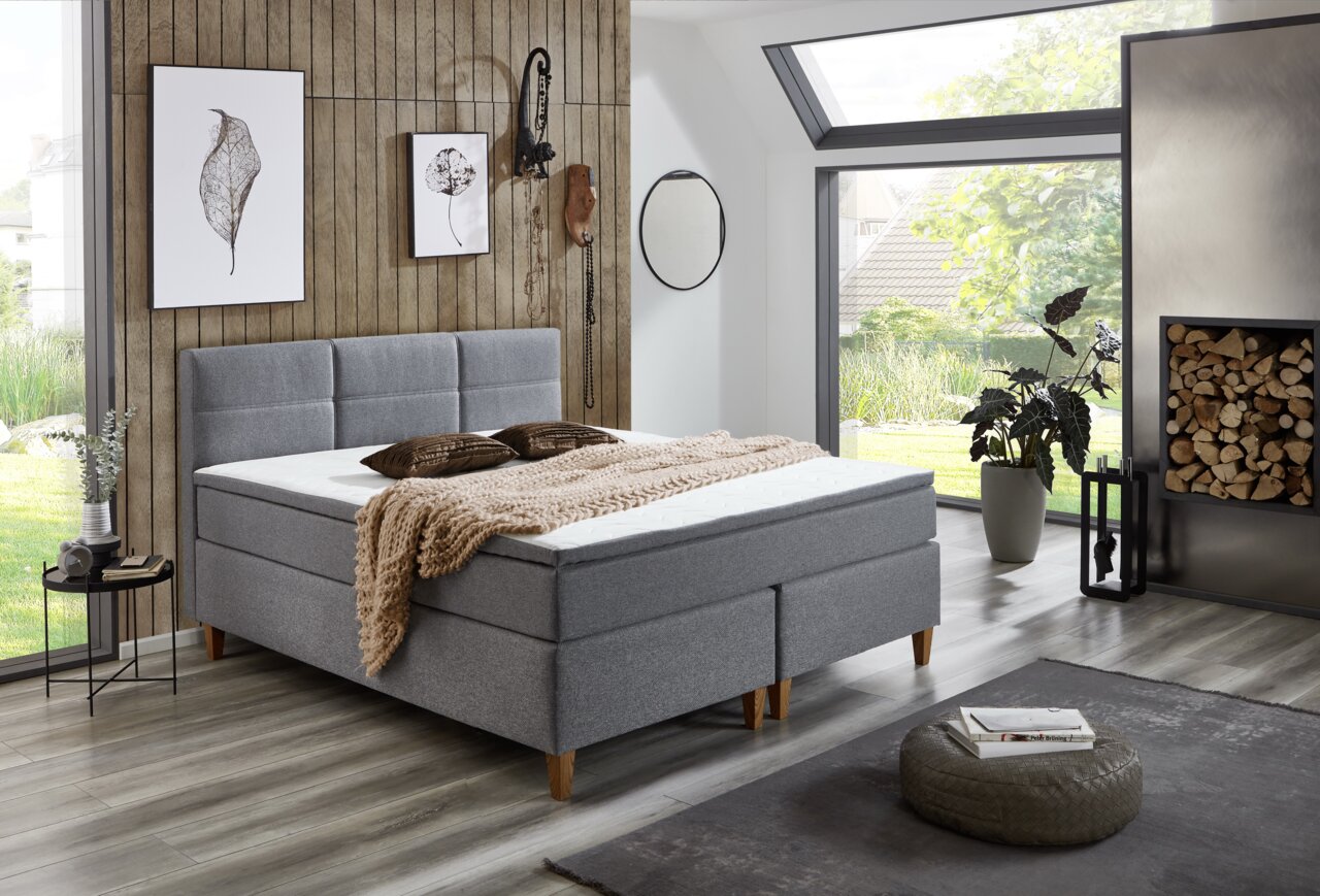 Modernes Boxspringbett in einem stilvollen Schlafzimmer mit Holzverkleidung und großen Fenstern, seitliche Perspektive.