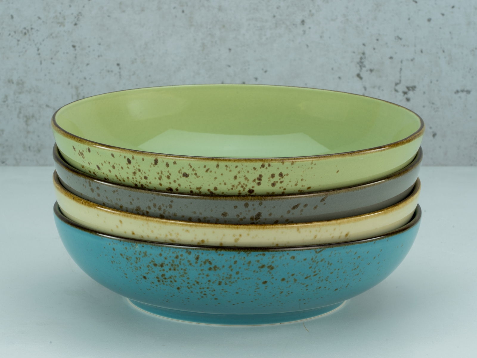 Vier stapelbare Poke Bowls in verschiedenen Farben, von der Seite betrachtet, auf einer hellen Oberfläche vor einer grauen Wand.