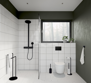 Moderne Badezimmeransicht mit schwarzer WC-Bürste aus Stahl neben einer Toilette, umgeben von weißen Fliesen und grünen Wänden.