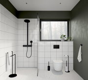 Moderne Badezimmeransicht mit schwarzer WC-Bürste aus Stahl neben einer Toilette, umgeben von weißen Fliesen und grünen Wänden.