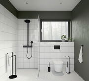 Moderne Badezimmeransicht mit schwarzer WC-Bürste aus Stahl neben einer Toilette, umgeben von weißen Fliesen und grünen Wänden.