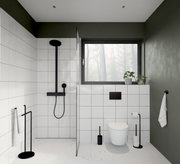 Moderne Badezimmeransicht mit schwarzer WC-Bürste aus Stahl neben einer Toilette, umgeben von weißen Fliesen und grünen Wänden.