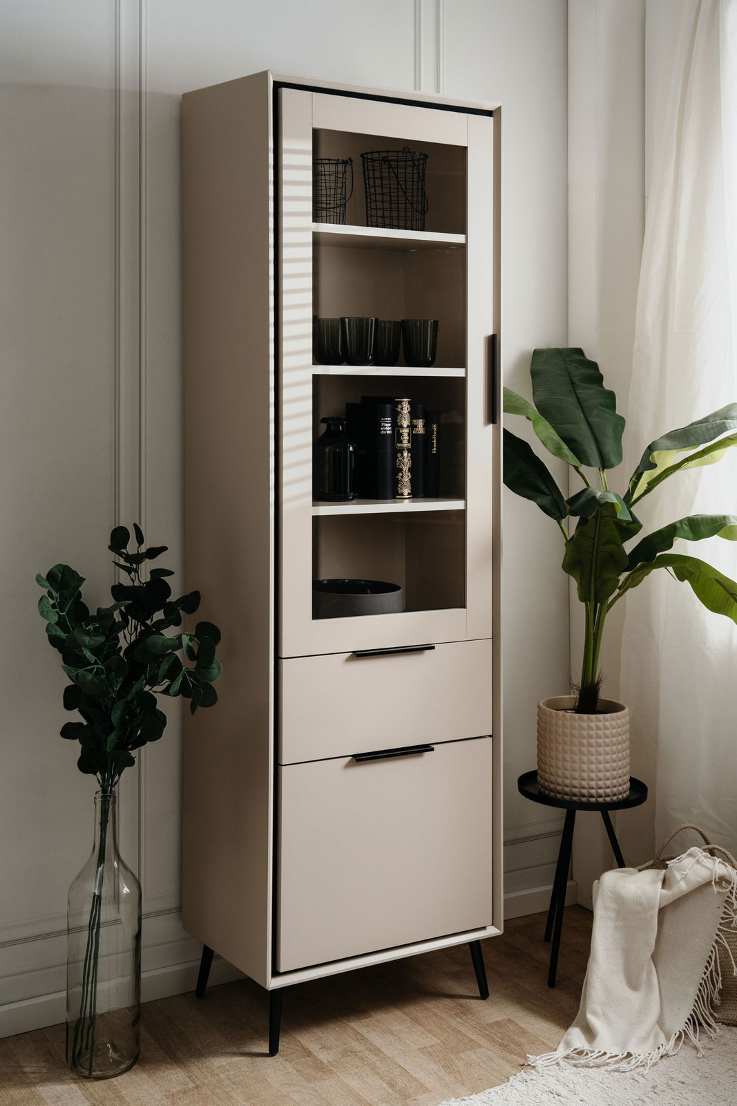 Moderne Vitrine mit Glastür und Schubladen, seitliche Perspektive, dekoriert mit Pflanzen und Accessoires.