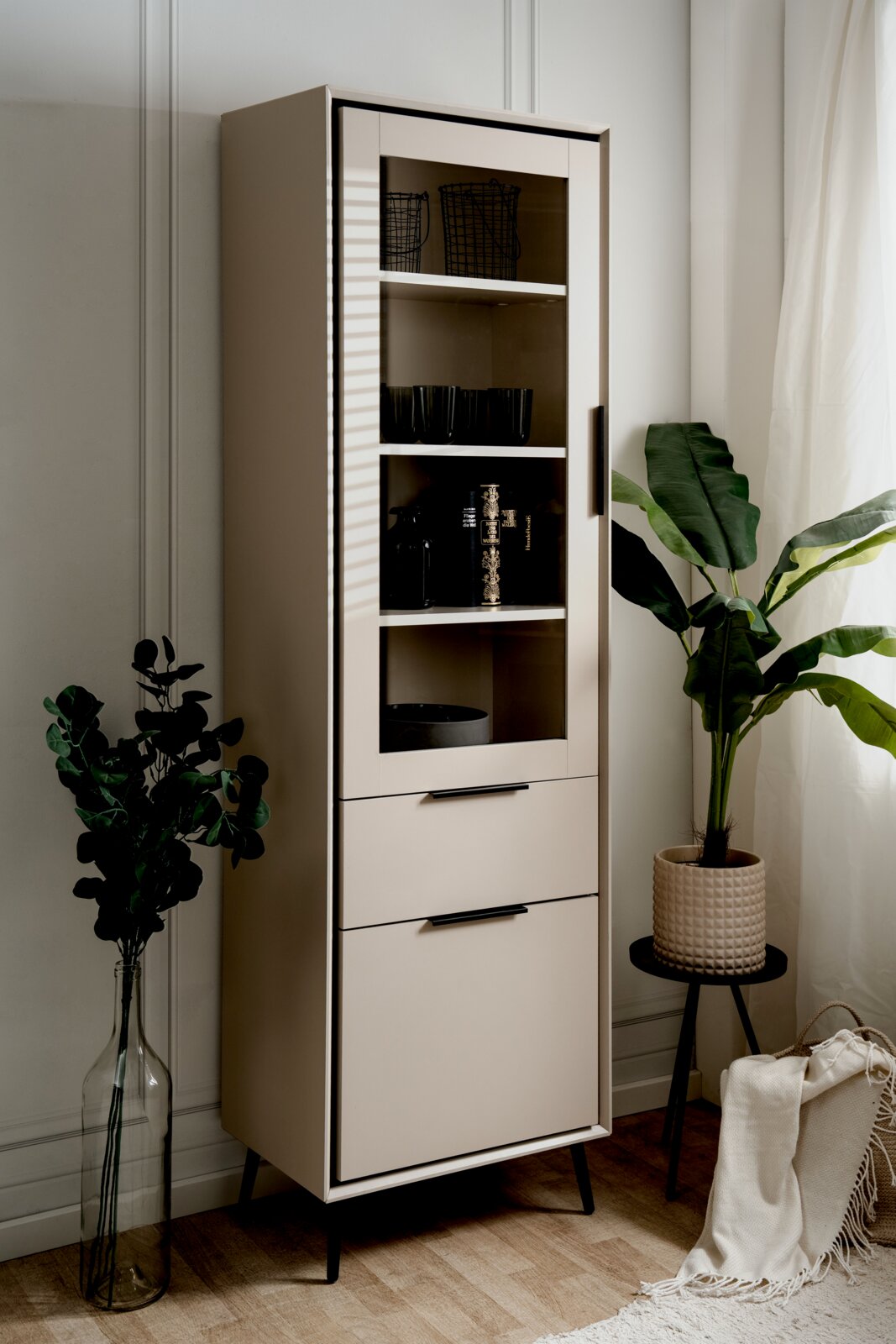 Moderne Vitrine mit Glastür und Schubladen, seitliche Perspektive, dekoriert mit Pflanzen und Accessoires.