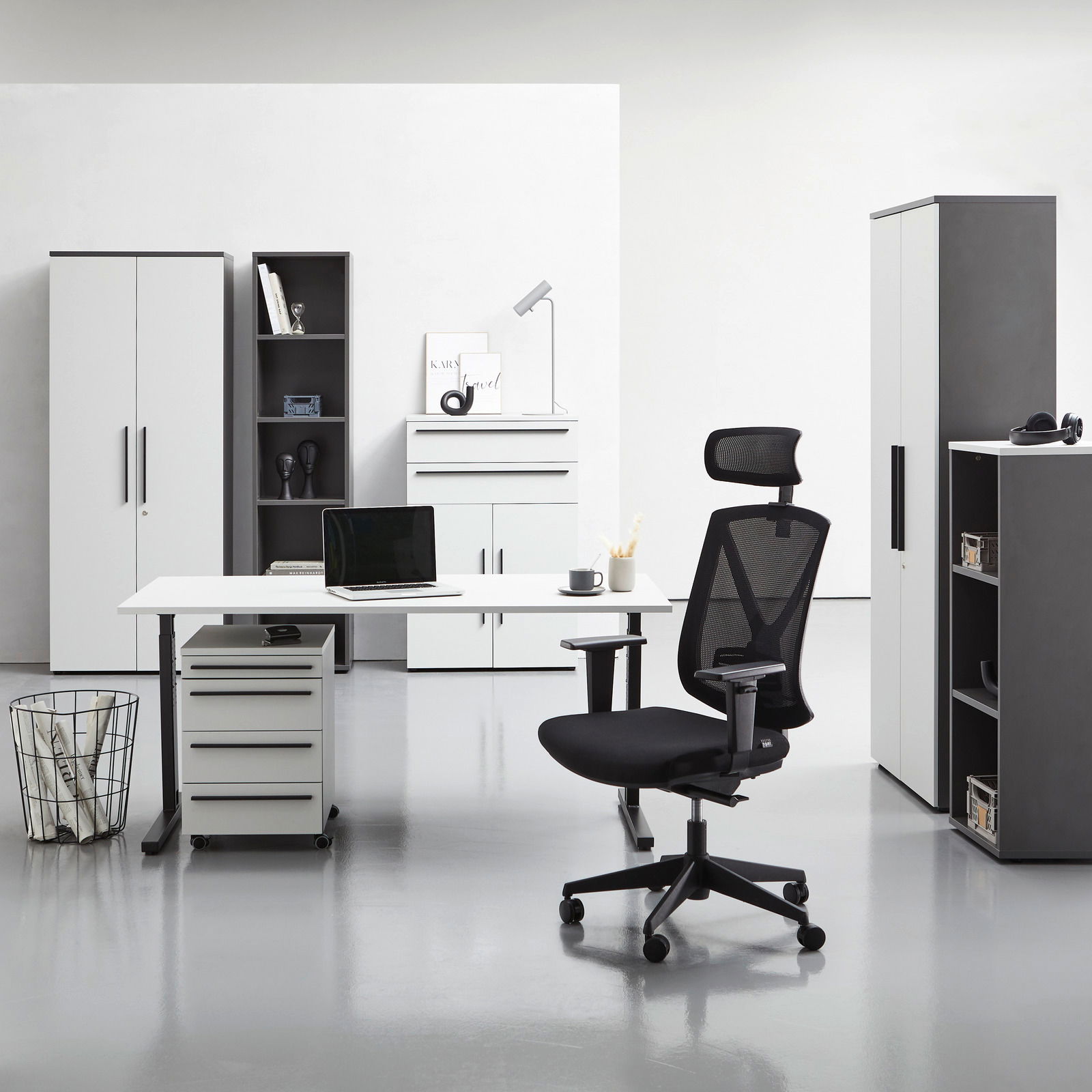 Moderne Büromöbel in einem hellen Raum, darunter ein Winkelschreibtisch, Rollcontainer, Aktenschränke und ein ergonomischer Bürostuhl. Frontalansicht.