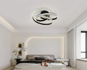 Moderne LED-Deckenleuchte in Schwarz mit drei überlappenden, leuchtenden Ringen in warmweiß, montiert an der Zimmerdecke; Perspektive: leicht von unten im Schlafzimmer aufgenommen.