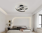 Moderne LED-Deckenleuchte in Schwarz mit drei überlappenden, leuchtenden Ringen in warmweiß, montiert an der Zimmerdecke; Perspektive: leicht von unten im Schlafzimmer aufgenommen.