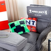 Grauer Minecraft-Gaming-Sessel mit bestickter Rückenlehne „MINECRAFT – Mine. Naa. Repeat.“ und zwei Minecraft-Kissen (Creeper und Pixelmotiv), fotografiert in schräger Vorderansicht von oben.