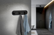 Dreierhaken aus schwarzem Edelstahl an einer Badezimmerwand, frontal betrachtet, mit zwei aufgehängten Handtüchern in Grau und Blau.