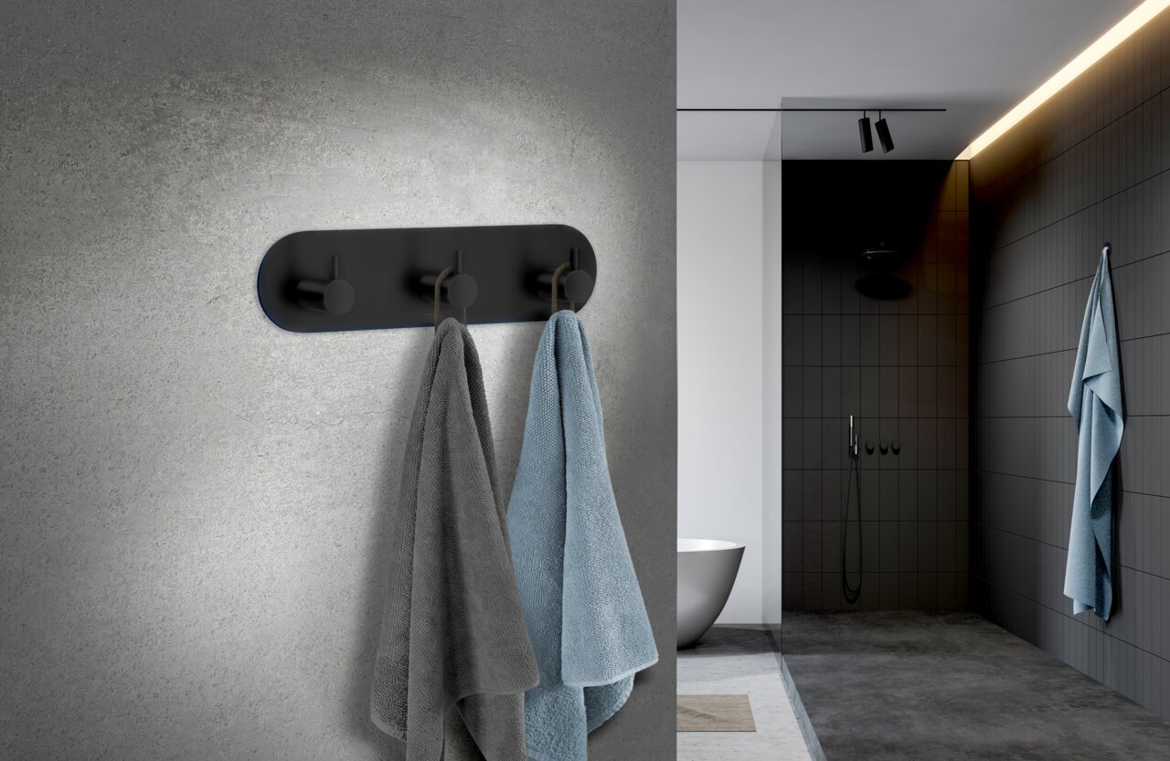 Dreierhaken aus schwarzem Edelstahl an einer Badezimmerwand, frontal betrachtet, mit zwei aufgehängten Handtüchern in Grau und Blau.