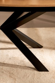 Detailaufnahme in leichter Untersicht: schwarzes, X-förmiges Metall-Tischgestell unter einer Holz-Tischplatte auf hellem Teppich