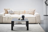 Moderner schwarzer Beistelltisch aus Metall, frontal vor einem cremefarbenen Sofa mit dekorativen Kissen und einer Decke, auf einem hellen Teppich.