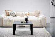 Moderner schwarzer Beistelltisch aus Metall, frontal vor einem cremefarbenen Sofa mit dekorativen Kissen und einer Decke, auf einem hellen Teppich.