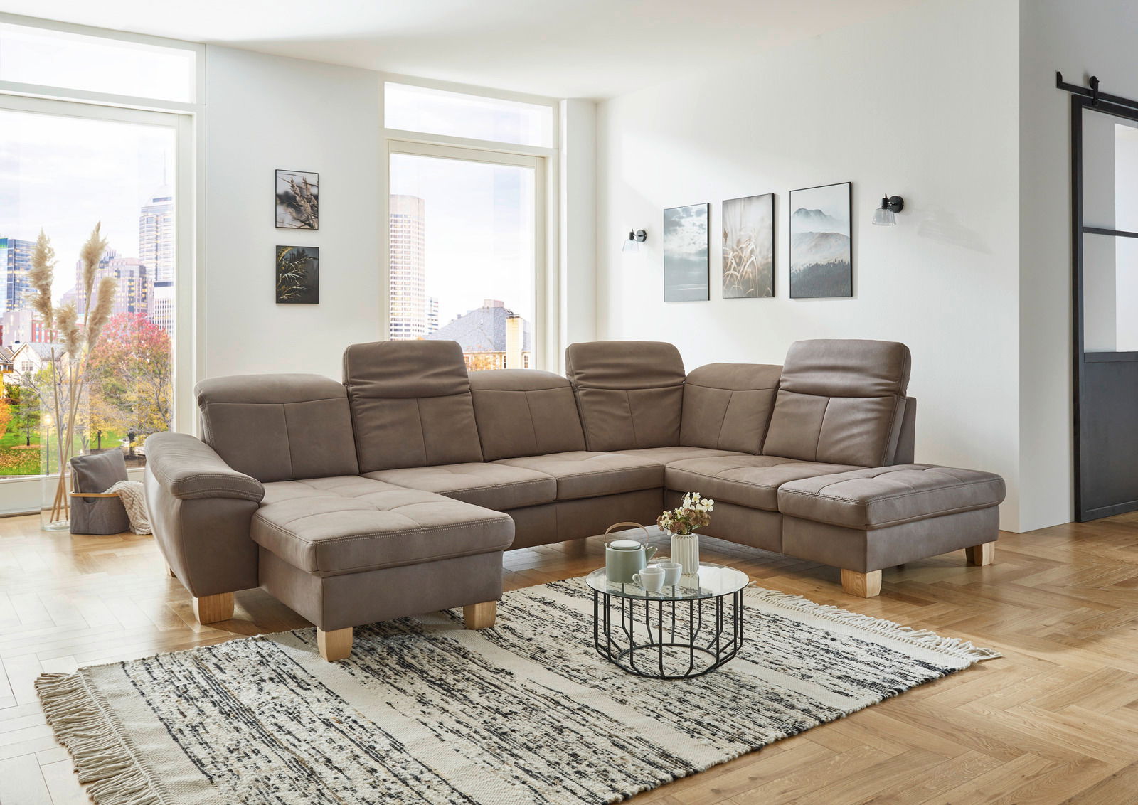 Moderne Polsterrundecke in einem hellen Wohnzimmer mit großen Fenstern, aus der Perspektive von vorne links betrachtet.