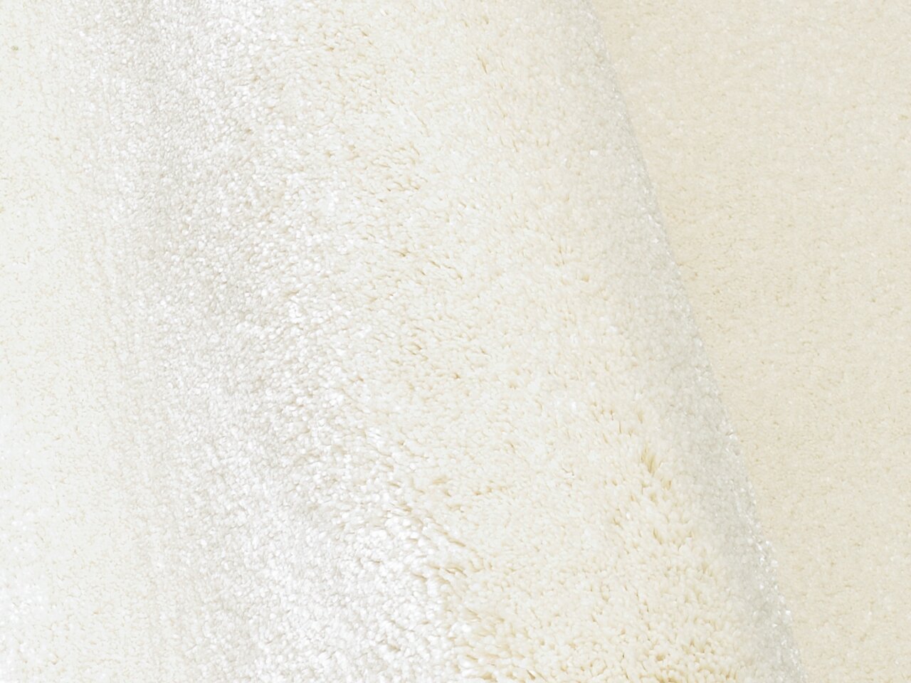 Nahaufnahme eines cremeweißen Uni-Teppichs mit weicher Textur, seitliche Perspektive