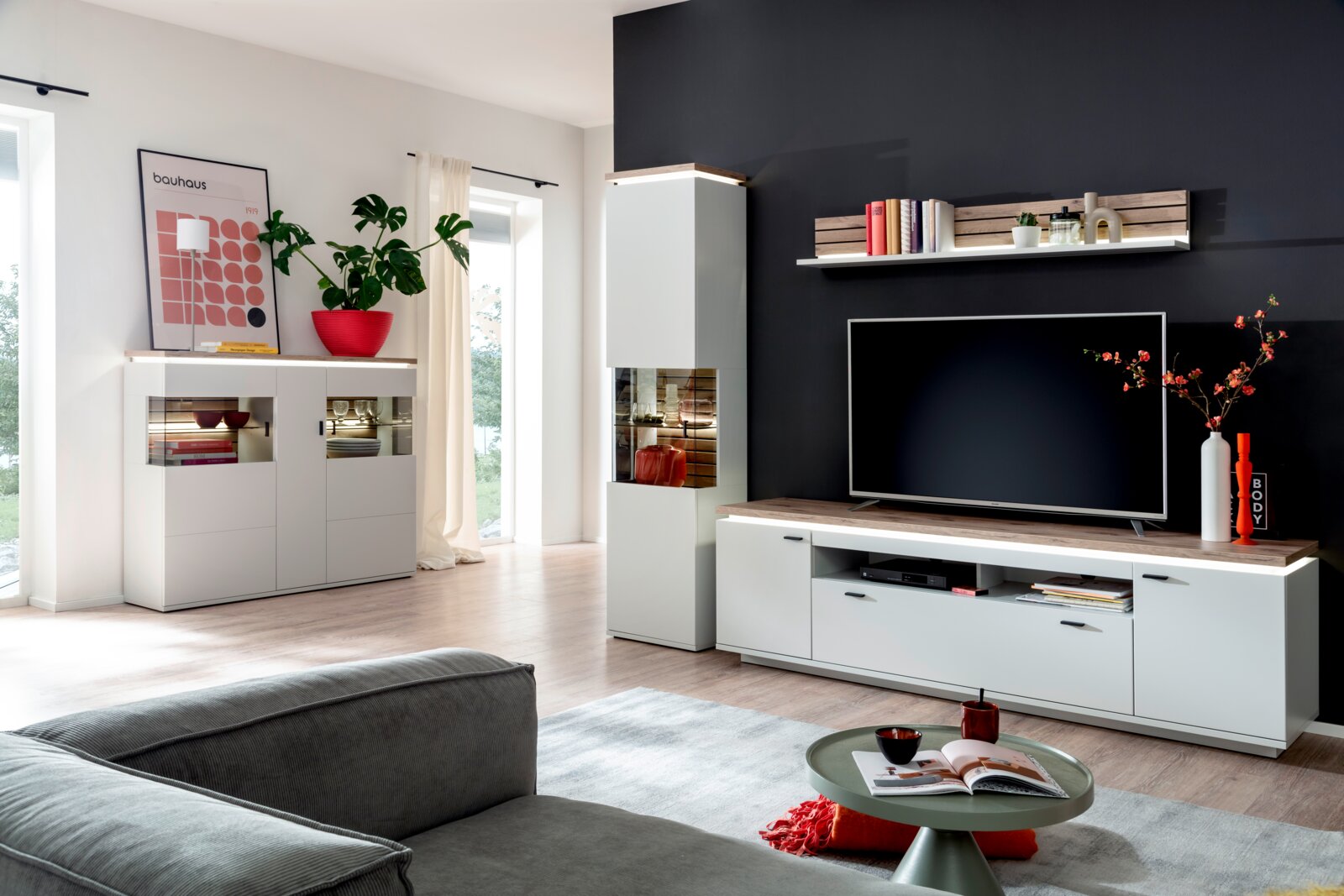 Stylife TV-Lowboard ESTEPONA Modernes Wohnzimmer mit weißer Wohnwand: TV-Lowboard mit Holzoptik-Abdeckung, Hängeregal und Vitrinenschrank mit Glasfront, aufgenommen in leichter Schrägansicht von vorn.