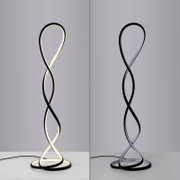 Moderne LED-Stehleuchte in geschwungener, gedrehter Schleifenform mit schwarzem Rahmen und integriertem Lichtband, frontale Ansicht auf neutralem Hintergrund; links eingeschaltet mit warmweißem Licht, rechts ausgeschaltet.