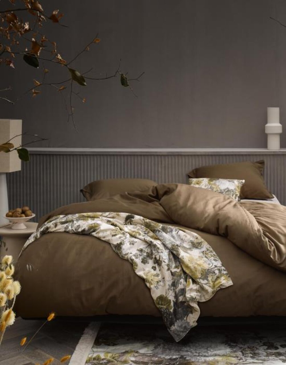 Gemütliches Schlafzimmer mit einer stilvollen Tagesdecke in Erdtönen und floralen Mustern, seitliche Perspektive.