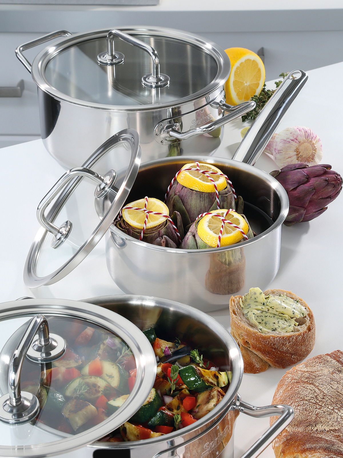 Topfset Brigade Basic 5-tlg. aus Edelstahl, gefüllt mit frischem Gemüse und Artischocken, auf einer Küchenarbeitsplatte von oben fotografiert.