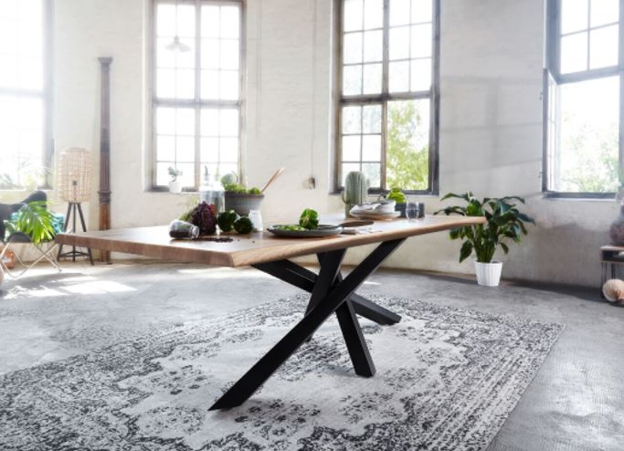 Moderne houten eettafel met een zwart kruisonderstel, zijaanzicht in een lichte ruimte met grote ramen.