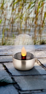 Tuinlamp op zonne-energie met vlamvormige lichtbundel, geplaatst op een stenen vloer in de open lucht, zijaanzicht.