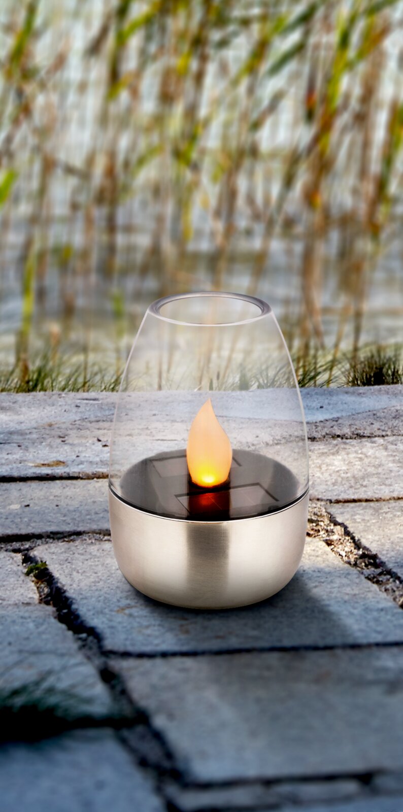 Tuinlamp op zonne-energie met vlamvormige lichtbundel, geplaatst op een stenen vloer in de open lucht, zijaanzicht.