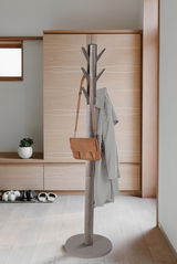 Moderner Garderobenständer aus Metall mit mehreren Haken, auf denen ein Mantel und eine Tasche hängen. Perspektive: Frontalansicht in einem minimalistischen Raum.