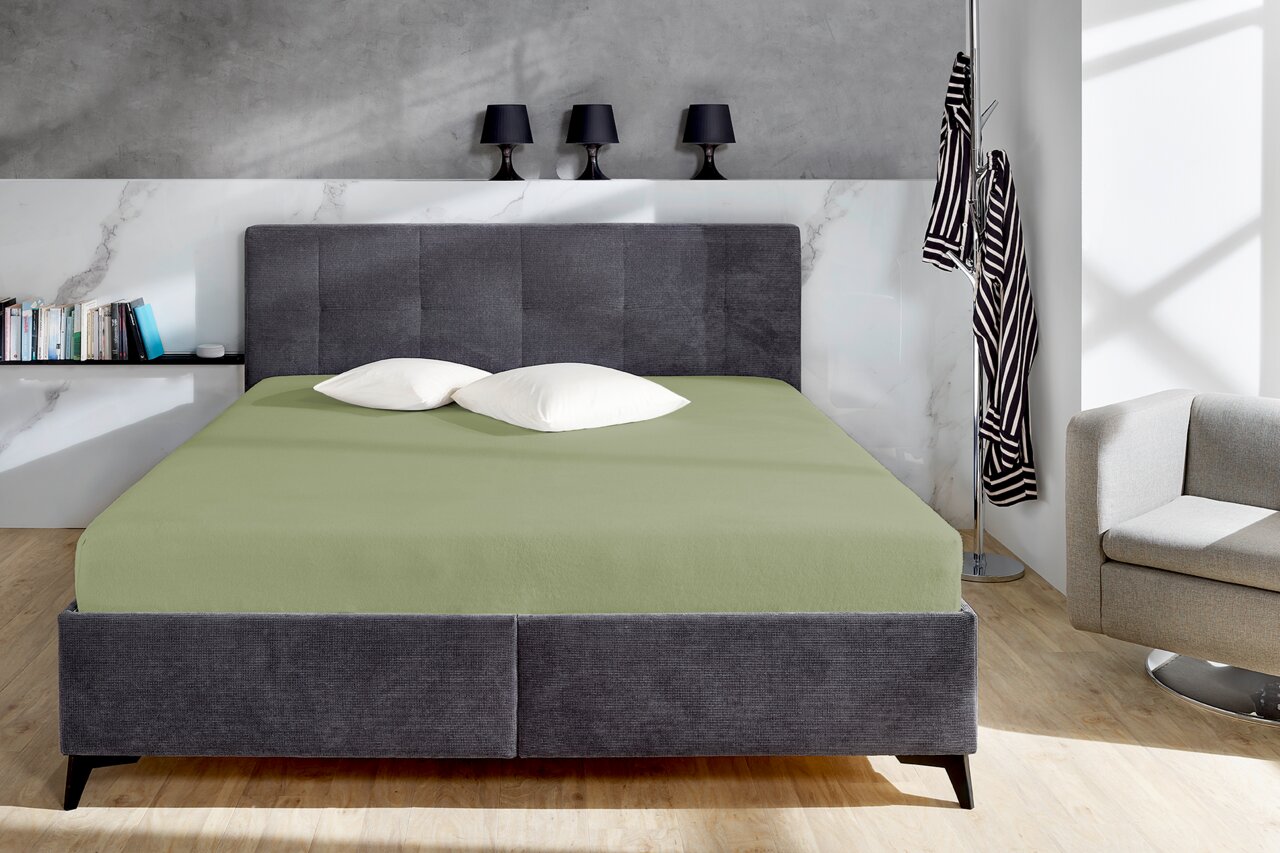 Grünes Spannbetttuch auf einem grauen Bett in einem modernen Schlafzimmer, frontal aufgenommen.