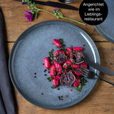 Blauer Teller mit elegant angerichtetem Essen, fotografiert aus der Vogelperspektive.