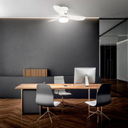 Moderner weißer Deckenventilator mit integrierter LED-Leuchte in einem minimalistischen Büro über einem Holztisch, Frontalansicht leicht von unten.