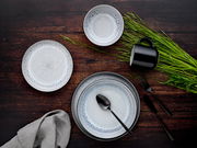 Vogelperspektive auf ein stilvolles Kombiservice-Set mit 30 Teilen in Frost-Design, bestehend aus Tellern, Schalen und einer Tasse auf einem dunklen Holztisch, dekoriert mit grünem Gras und schwarzem Besteck.