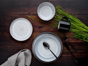 Vogelperspektive auf ein stilvolles Kombiservice-Set mit 30 Teilen in Frost-Design, bestehend aus Tellern, Schalen und einer Tasse auf einem dunklen Holztisch, dekoriert mit grünem Gras und schwarzem Besteck.