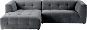 Graues, gepolstertes Ecksofa mit linksseitiger Ottomane/Chaiselongue und quadratischer Steppung, freigestellt auf weißem Hintergrund, Ansicht schräg von vorne.