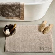 Badematte in Beige vor einer Badewanne, mit einem Korb und Hausschuhen daneben, von oben betrachtet.