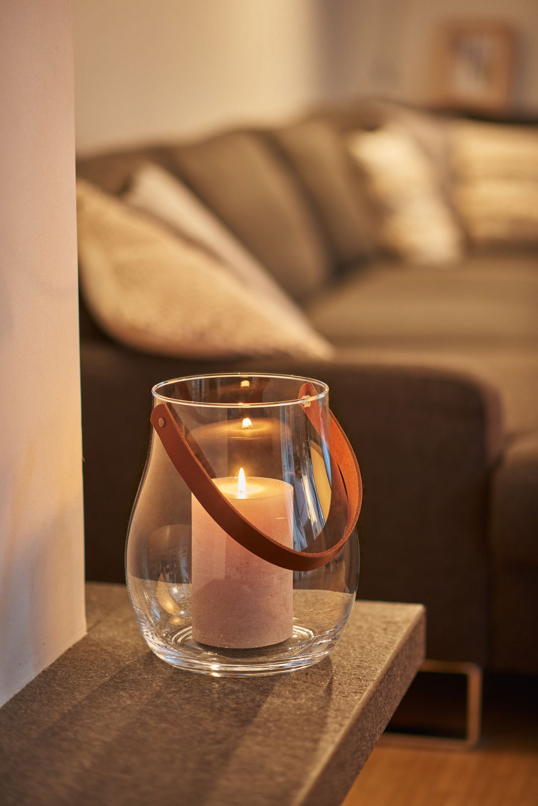 Windlicht mit Lederhenkel und brennender Kerze auf einem Tisch, seitliche Perspektive
