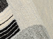 Nahaufnahme eines Webteppichs mit abstraktem Muster in Schwarz, Grau und Cremefarben, perspektivisch von oben fotografiert.