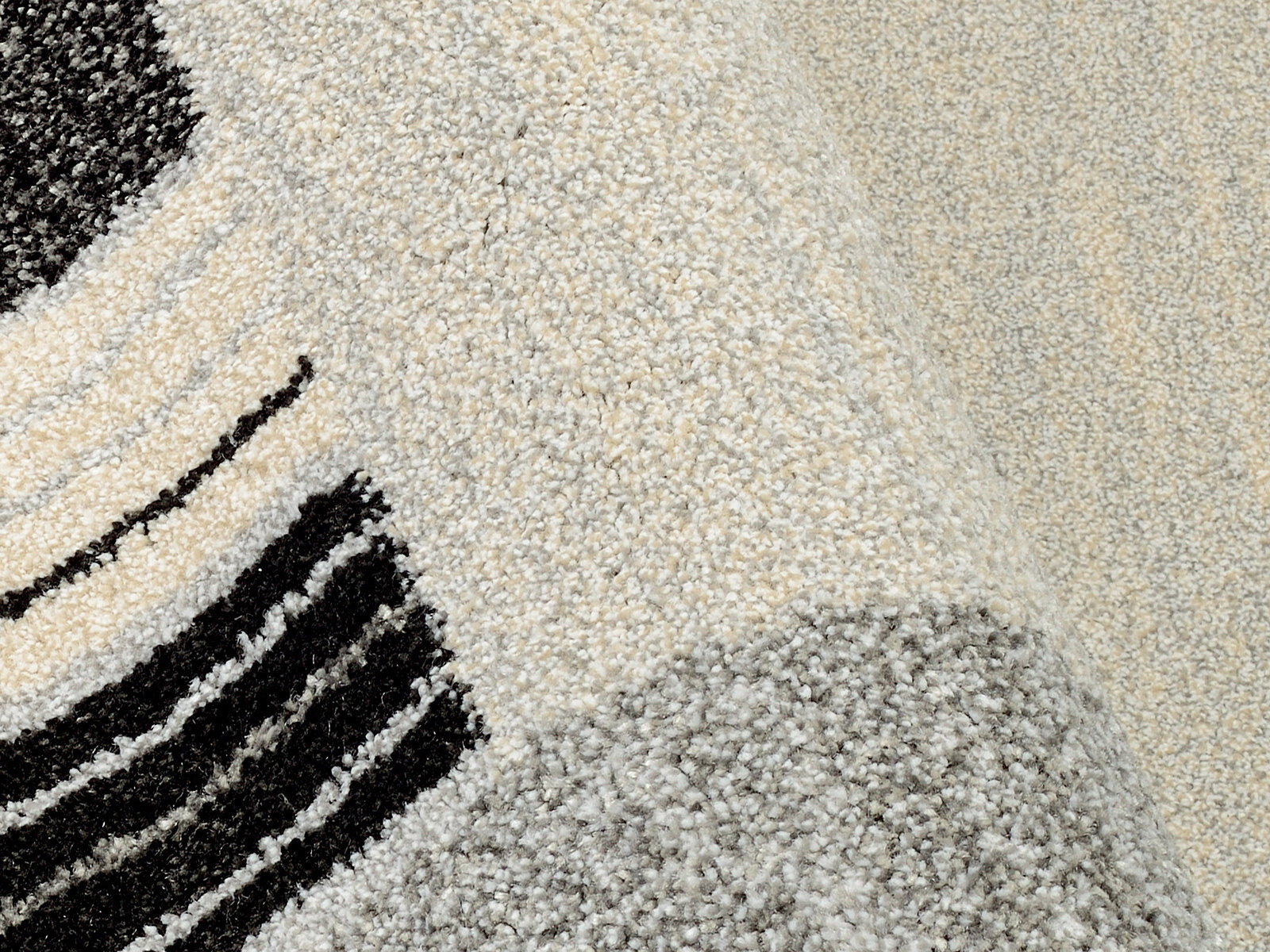 Nahaufnahme eines Webteppichs mit abstraktem Muster in Schwarz, Grau und Cremefarben, perspektivisch von oben fotografiert.