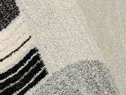 Nahaufnahme eines Webteppichs mit abstraktem Muster in Schwarz, Grau und Cremefarben, perspektivisch von oben fotografiert.