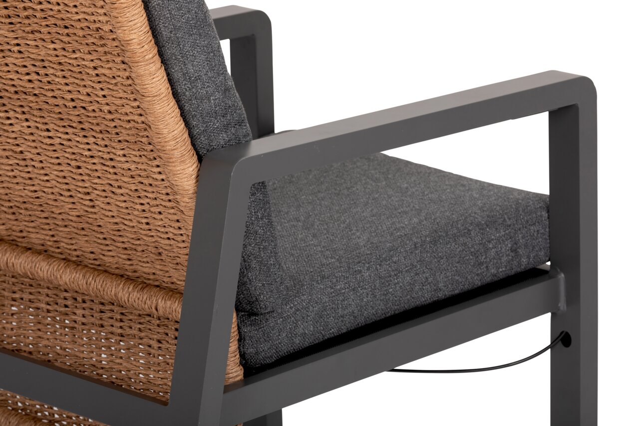 Detailansicht eines Loungesessels mit grauem Metallrahmen, grauem Kissen und geflochtener Rückenlehne aus Naturmaterial.
